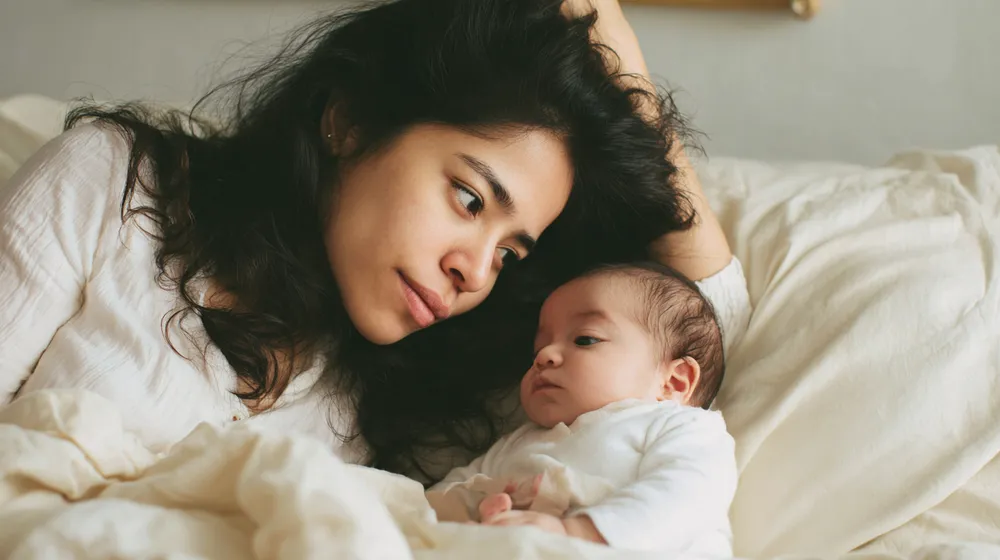 Mamá recostada mirando con ternura a su bebé recién nacido