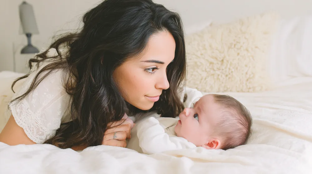Mamá y bebé recostados mirándose en la cama